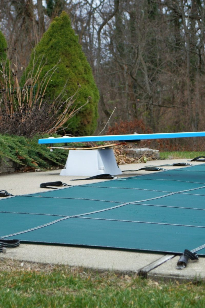 backyard swimming pool with diving board and pool slide tarped up and closed down for winter